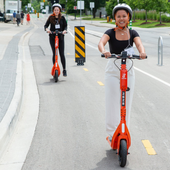 Two females riding e-scooters.