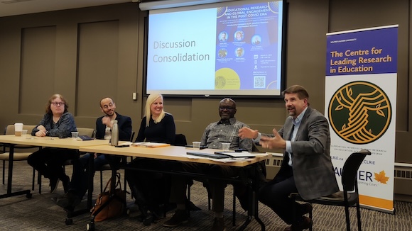 Discussion panel at an event, with members sitting at a table in front of a projector screen