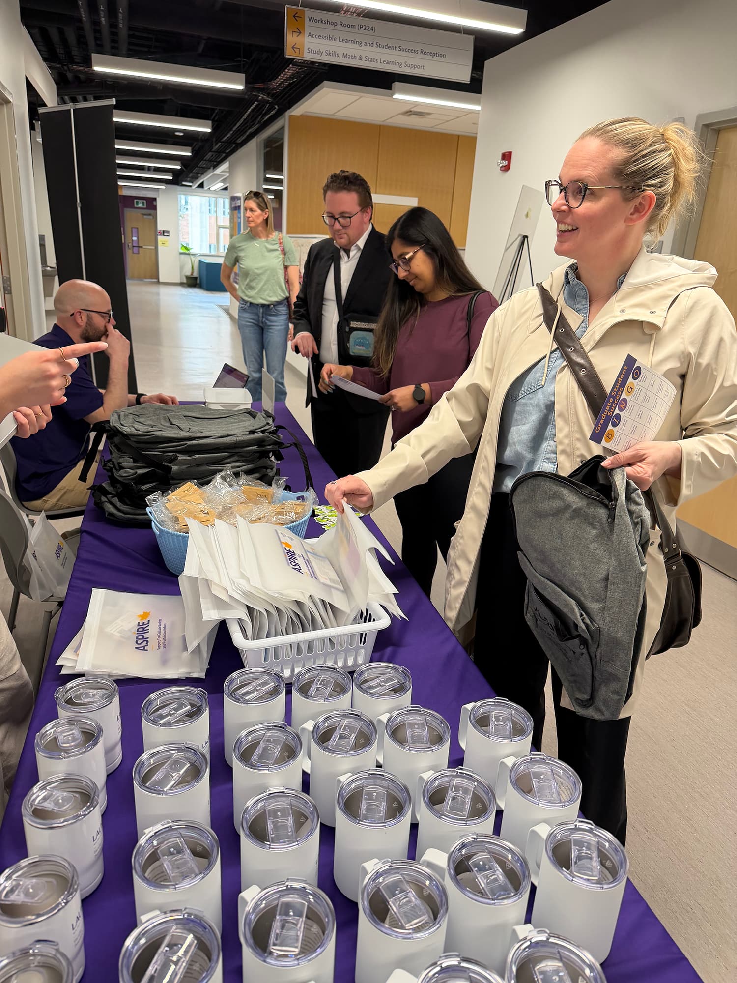 Students collecting ASPIRE swag from a table with bags, mugs, etc.
