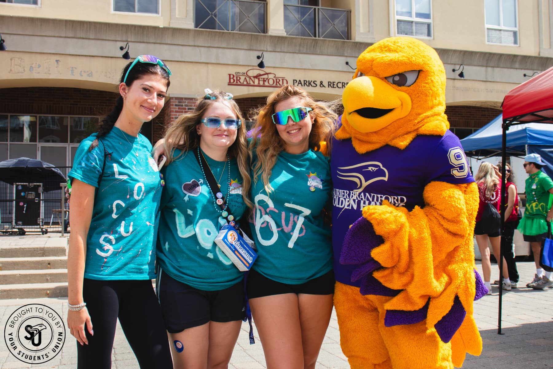 Three students in LOCUS shirts standing with Midas the Golden Hawk