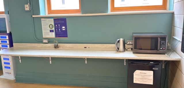 A shelf with a microwave, kettle and small fridge