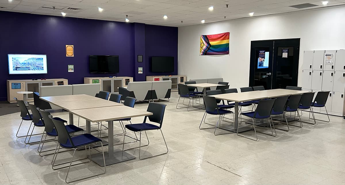 Rows of desk space, couches facing tvs on consoles, lockers and a progressive pride flag handing on the wall