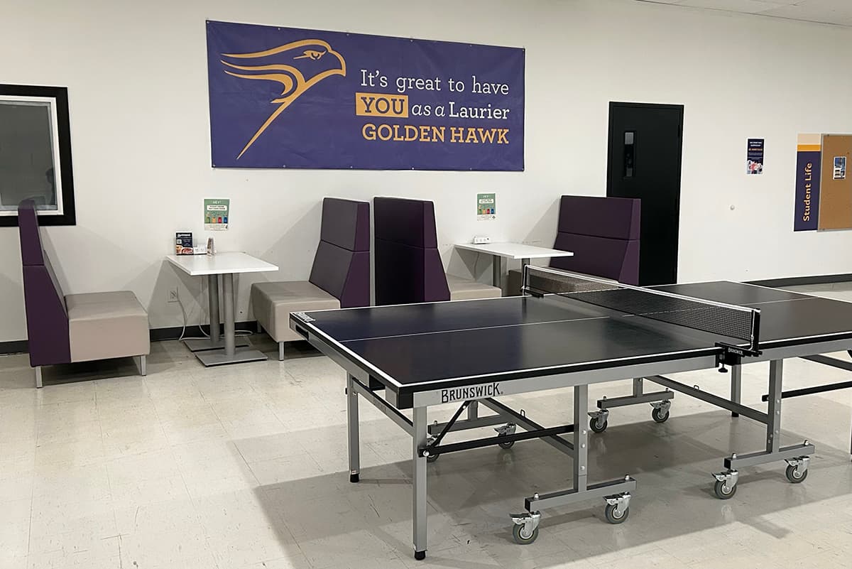 Ping pong table next to a row of booth seating against a wall with a golden hawk banner
