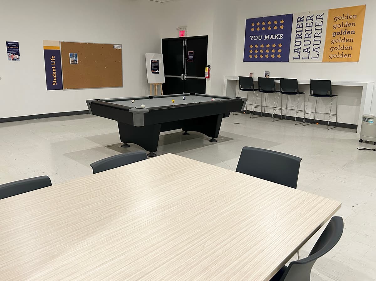 A pool table and desk seating in front a wall with a cork board and Laurier banners