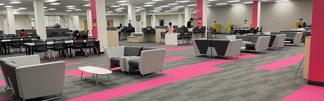 A row of lounge seating chairs around coffee tables with rows of desks in the background