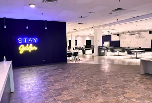 Foyer with tiled floor leading into a room full of tables with a Stay Golden florescent sign on a purple wall