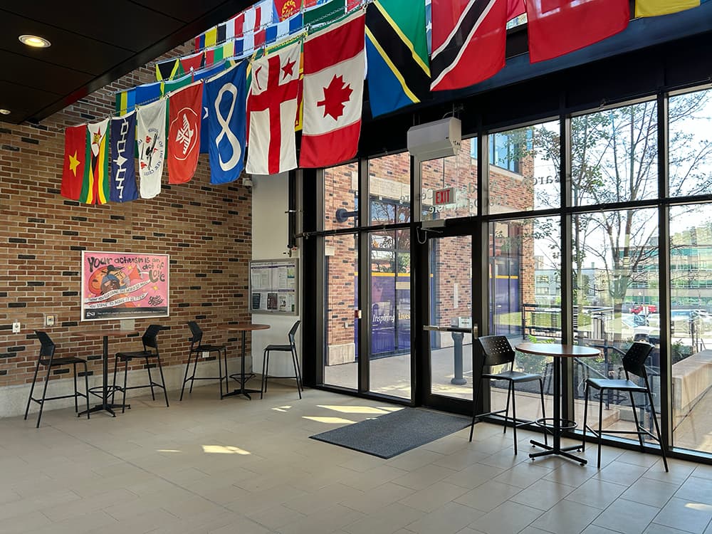 Glass doors leading to a lobby with tables and flags from around the world hanging down