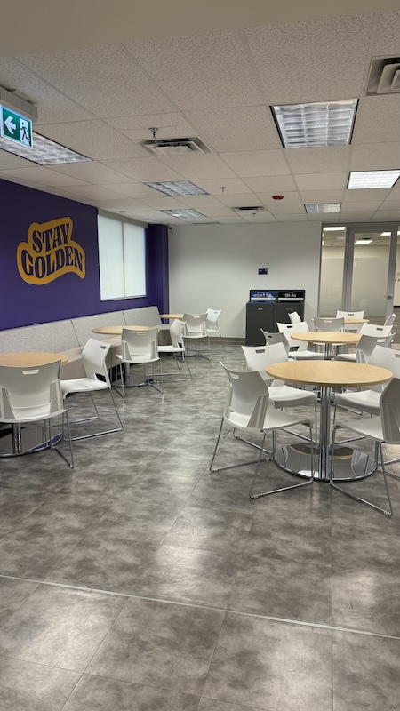 A large room with rows of tables and bench seating along a wall that says 'Stay Golden'