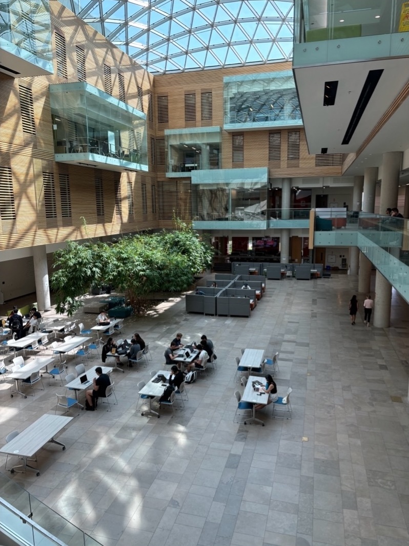 Open atrium with tables and cubicles on the ground floor, a glass balcony and glass study rooms on the upper floors
