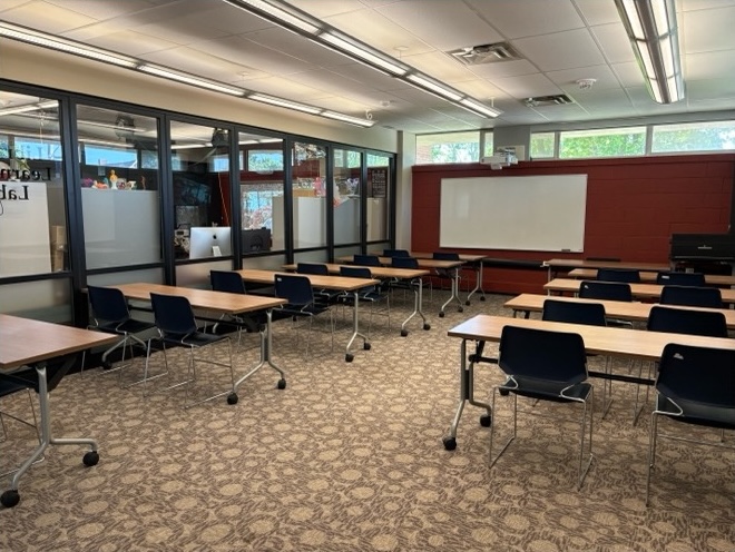 A room full of desks with a white board on the back wall