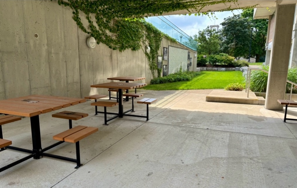 Concrete area with patio tables, with ivy and a memorial wall in the background