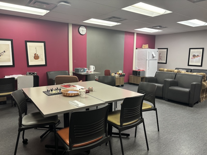 A large table in front of three rows of lounge chairs and kitchen appliances in the background