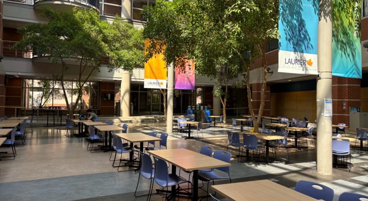 Open floor space with rows of tables between trees and pillars with Laurier banners