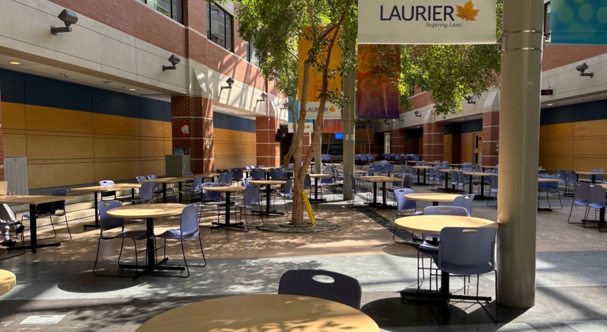 Atrium full of tables on the ground floor, around trees and pillars with Laurier banners