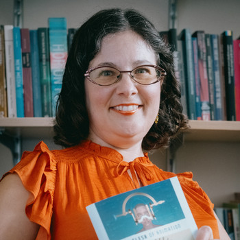Dr. Annett is shown wearing an orange shirt and holding a copy of her book The Flesh of Animation