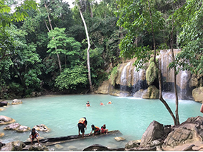 Tourists swimming in water below a waterfall