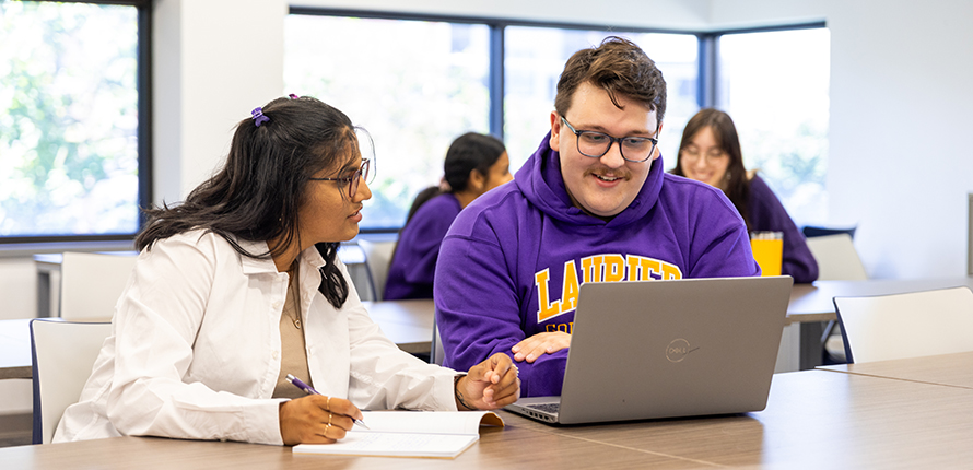Two students looking at a laptop in a classroom