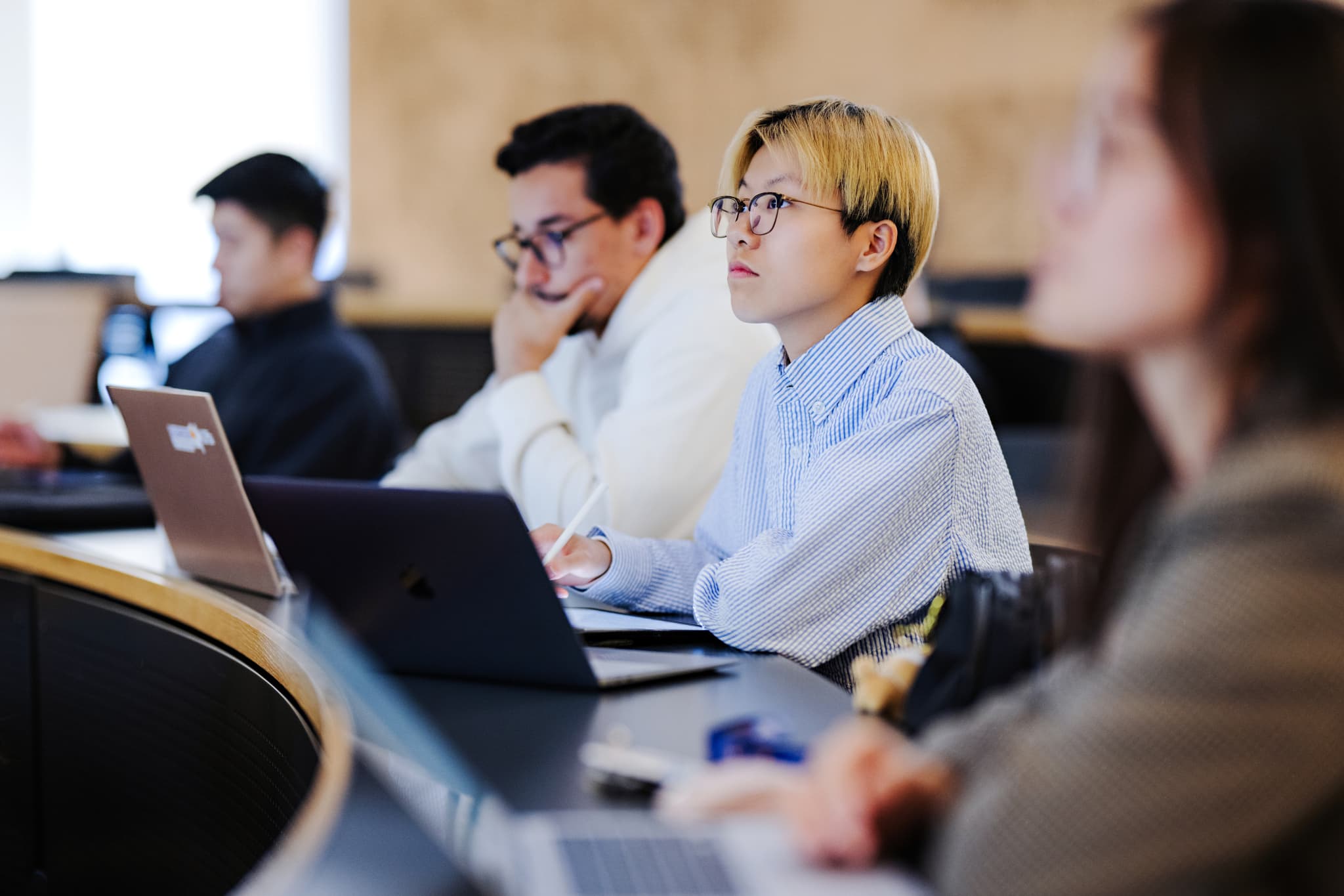 Students sat around tables with laptops with charts on projector screens in the background