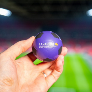 small purple soccer ball with Lazaridis School logo held in front of a soccer field