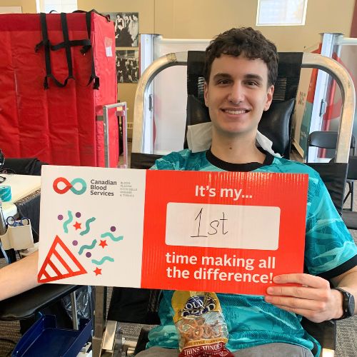 Young man sitting in a chair holding a sign that reads "It's my first time making a difference."