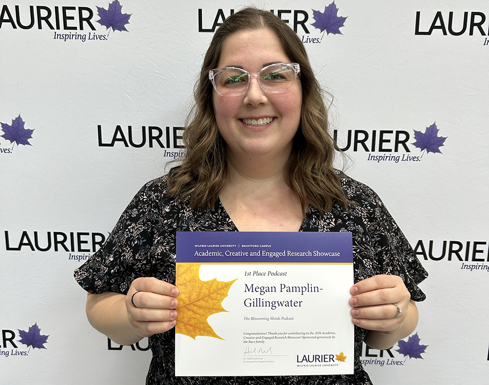 Megan Pamplin-Gillingwater holds her ACERS certificate in front of a Laurier-branded backdrop