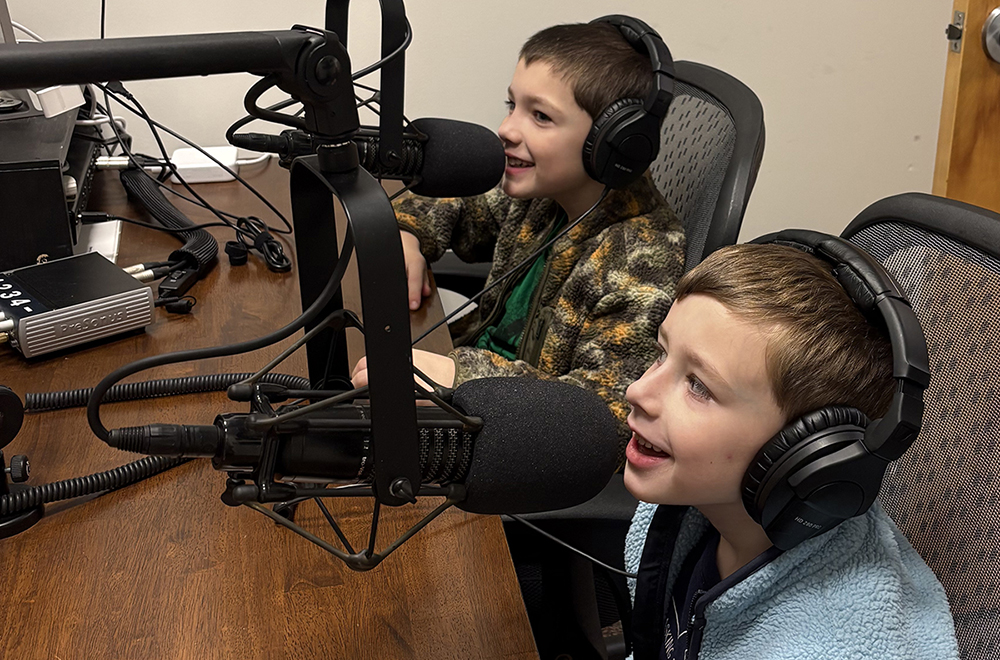 Two young boys sit in a podcast recording studio