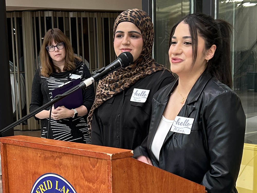 Mena Botros and Shiza Sajid stand at a podium