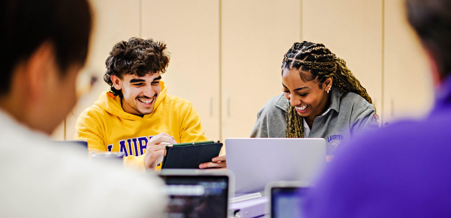 male and female students laughing looking at laptops