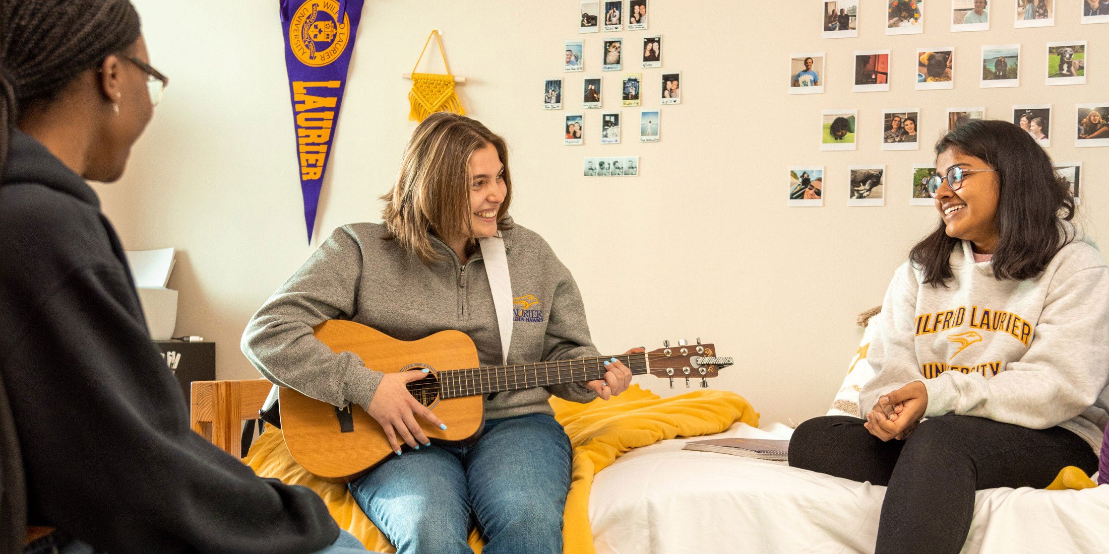 three female students playing guitar in dorm room