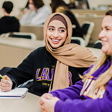 Student smiling at and conversing with another student in a classroom