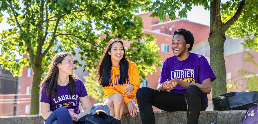 students smiling and sitting on campus in the summer