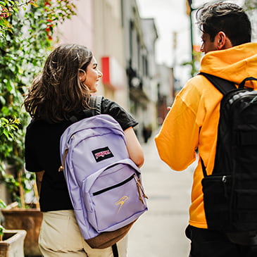 Two students wearing backpacks walking away from the camera in downtown Milton