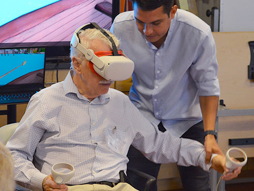 John Munoz guides a senior wearing VR goggles