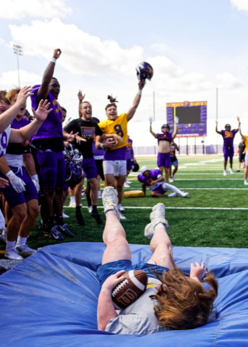 Woman jumps onto a crash mat holding a football.