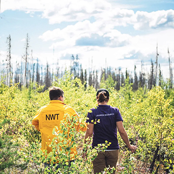 Man in a gold coat and woman in purple shirt walking through a forest