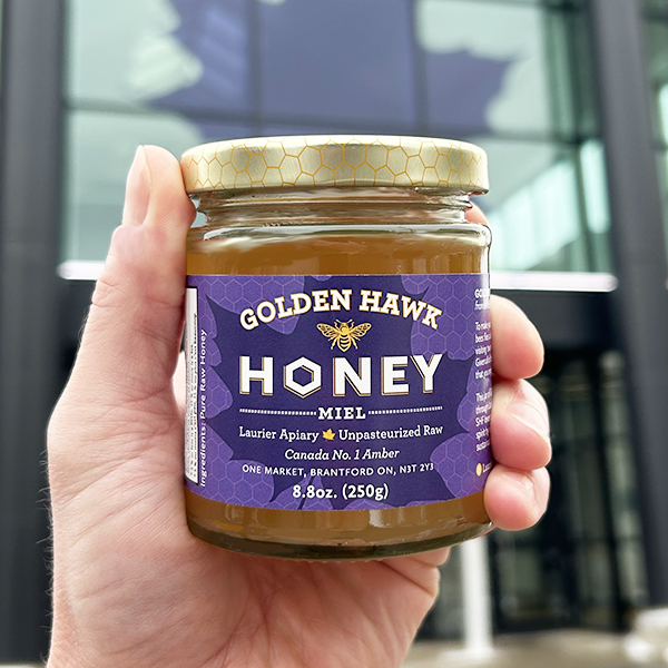 A jar of Golden Hawk Honey being held in front of the One Market building