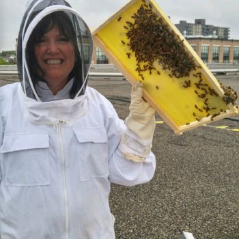 Richelle Monaghan in a beekeeper suit holding bees.