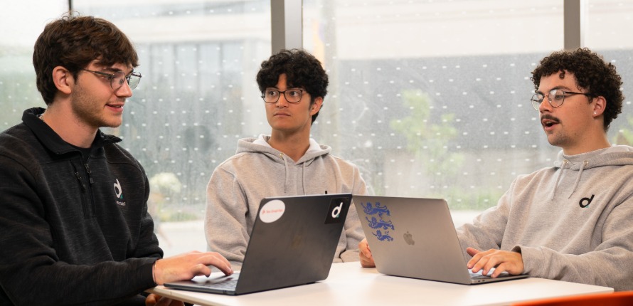 Three students sit at a table working