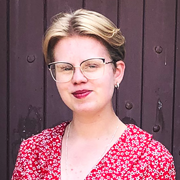 smiling student with glasses in front of wooden door