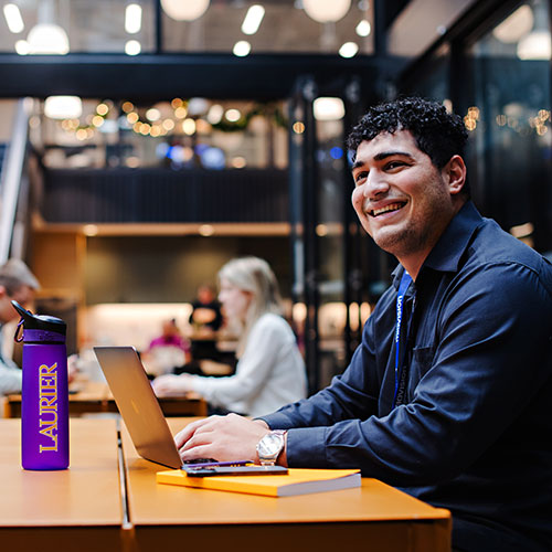 male student sitting at a table with laptop and smiling